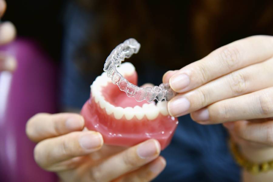 A dentist holding a clear Invisalign aligner next to a dental model of teeth.
