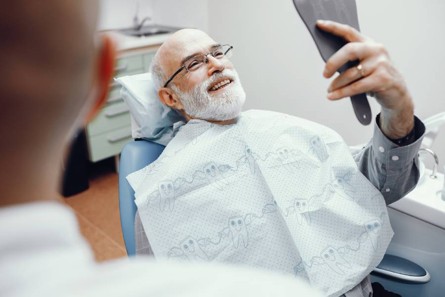 A senior man smiling while consulting with a dentist about dental implants and dentures.
